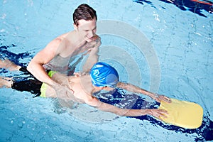 Male Swimming Coach Giving Boy Holding Float One To One Lesson In Pool