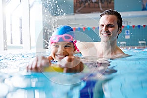 Male Swimming Coach Giving Girl Holding Float One To One Lesson In Pool photo