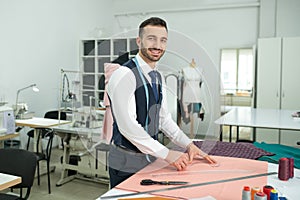 Male tailor outlining pattern on cloth, smiling