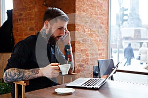 Male with tattoes talking on a phone in coffee shop