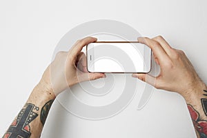 Male tattoo hand holding cell phone with empty screen on white background.