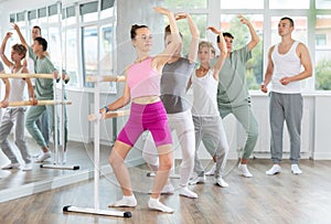 Male teacher conducts class with teens in ballet studio, observes doing plie exercise.