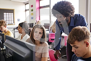 Male Teacher Helping Teenage Female High School Student Working In Computer Class