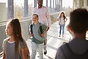 Male teacher and pupils walking in school campus