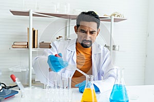 A male teacher in white lab coat with rubber gloves with many laboratory tools on shelves and table. Using pipette for drop
