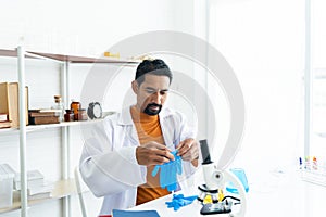 Male teacher in white lab coat wearing safety goggles wears rubber gloves. Shelves of various lab tools are being prepared with