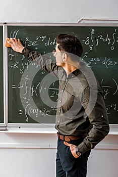 Male teacher wiping mathematical equations with sponge from chalkboard