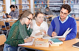 Male teacher working with young female students in university library