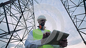 Male technician is browsing a computer while being near electricity towers