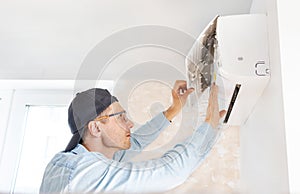 Male technician cleaning air conditioner indoors.