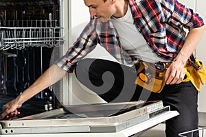 Male Technician Examining Dishwasher With Digital Multimeter