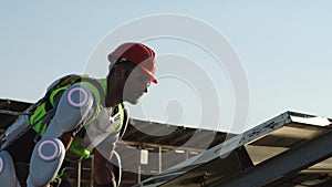 Male technician in exoskeleton installing solar cell with colleague