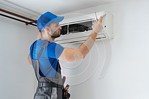 Samec technik v kombinéza a modrý čiapky opravy vzduch kondicionér na stena 