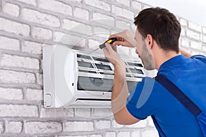 Male Technician Repairing Air Conditioner With Screwdriver