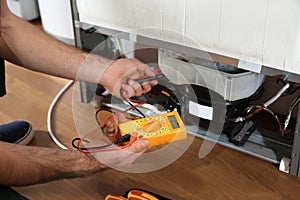 Male technician repairing broken refrigerator indoors