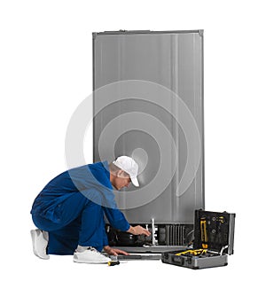 Male technician repairing refrigerator on background