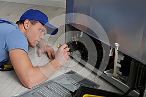 Male technician with screwdriver repairing refrigerator