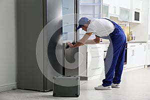 Male technician with screwdriver repairing refrigerator