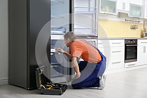 Male technician with screwdriver repairing refrigerator