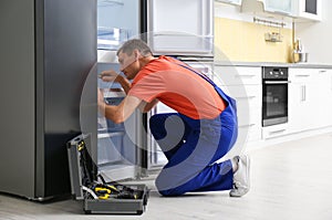 Male technician with screwdriver repairing refrigerator in kitchen