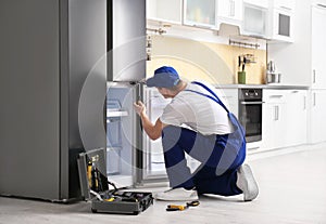 Male technician with screwdriver repairing refrigerator