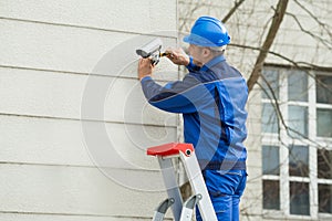 Male Technician Standing On Stepladder Fitting CCTV Camera