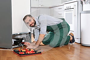 Male technician in uniform repairing refrigerator