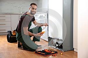 Male technician in uniform repairing refrigerator