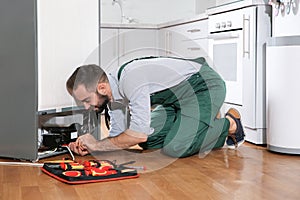 Male technician in uniform repairing refrigerator