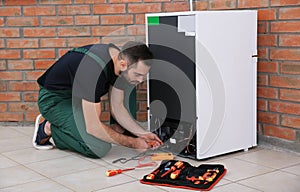 Male technician in uniform repairing refrigerator