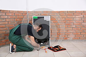 Male technician in uniform repairing refrigerator indoors.