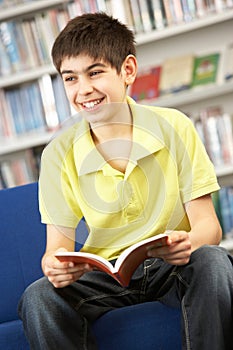 Male Teenage Student In Library Reading Book