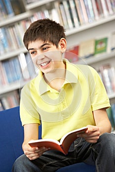 Male Teenage Student In Library Reading Book