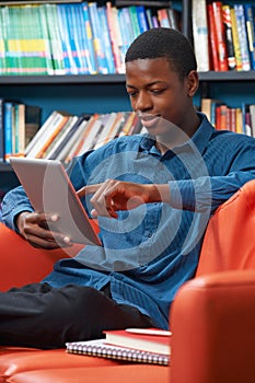 Male Teenage Student Using Digital Tablet In Library