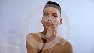Male teenager applying face cream, anti acne skin treatment, puberty period