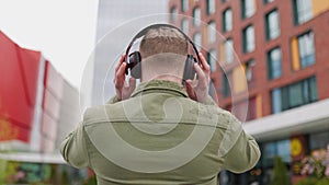 Male teenager with headphones listening to music, rear view. Young man enjoying music with rear view of cityscape