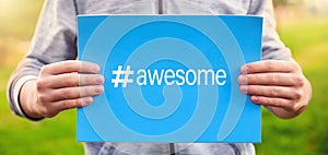 Male teenager holds a banner with the word awesome against nature background