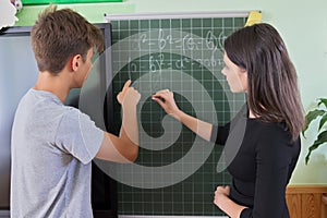 Male teenager student with teacher near school chalk board at math lesson