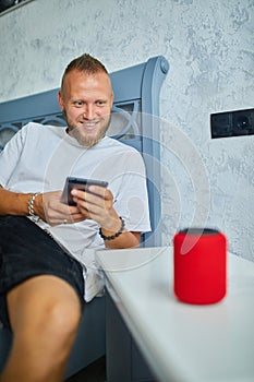 Male testing talking smart wireless speaker, man controlling home devices with a voice commands