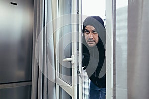 Male thief in black clothes trying to break the door lock in the house