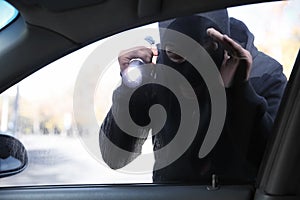 Male thief with flashlight looking inside car