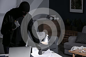 Male thief with flashlight  searching for documents indoors