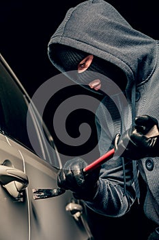Male thief is going to open the car door with a crowbar