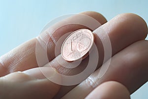 A male thumb and index finger gripping a one Euro cent Coin.