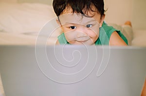 A male toddler is playing with a laptop while on the bed