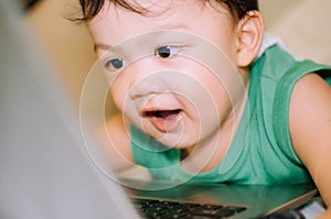 A male toddler is playing with a laptop while on the bed