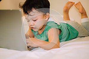 A male toddler is playing with a laptop while on the bed