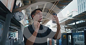 Male tourist with backpack making video call with smartphone while waiting for overground rail at city. Male tourist