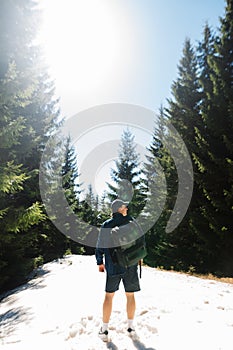 Male tourist in casual clothes with a backpack on his back stands in a snowy forest on a sunny spring day and looks away. Vertical