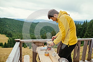 Male tourist in casual clothes preparing to eat at a table on the terrace of a country house in the mountains
